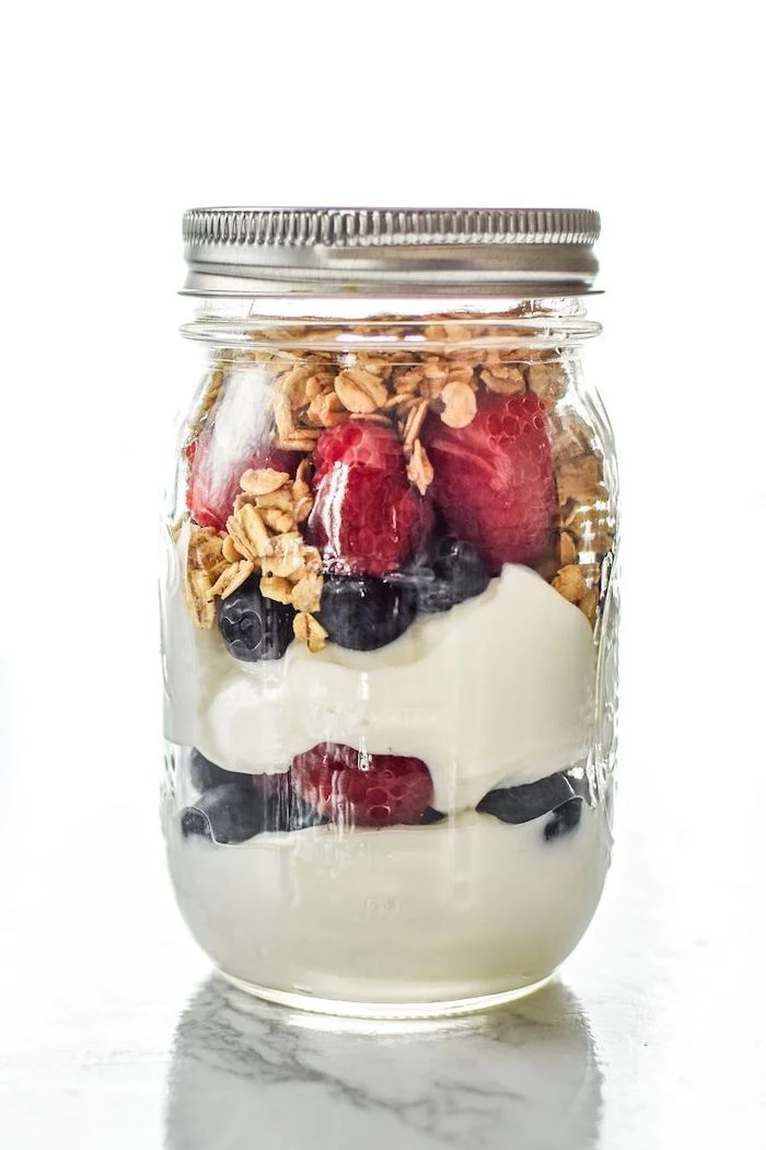 mason jar, filled with granola and yoghurt, raspberries and blueberries, meal prep, white background