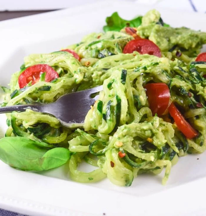 cherry tomatoes, zoodles with pesto, how to cook zucchini noodles, white plate, silver fork, basil leaves