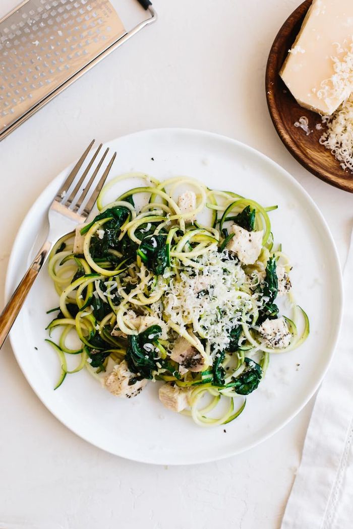 spinach and parmesan, chicken fillet, zucchini noodles, in a white plate, silver fork, white table