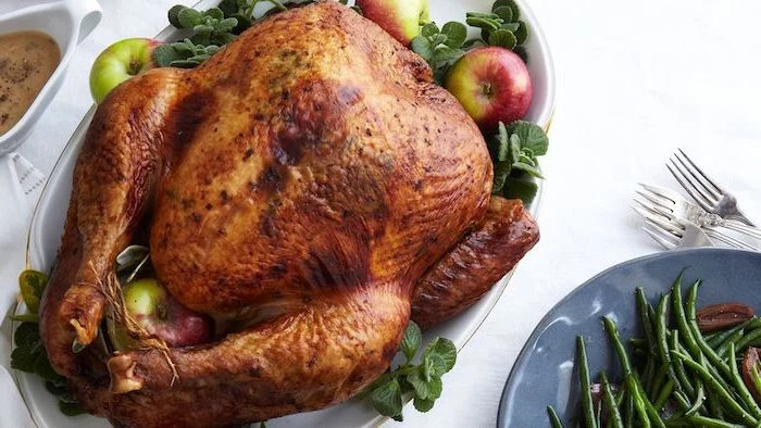 roasted turkey, fresh herbs, apples on the side, how to bake a turkey, white table, gravy in a jug