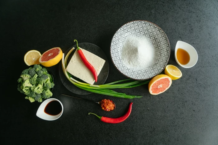 asian tofu, grapefruits and lemons, broccoli and soy sauce, ingredients spread on black countertop