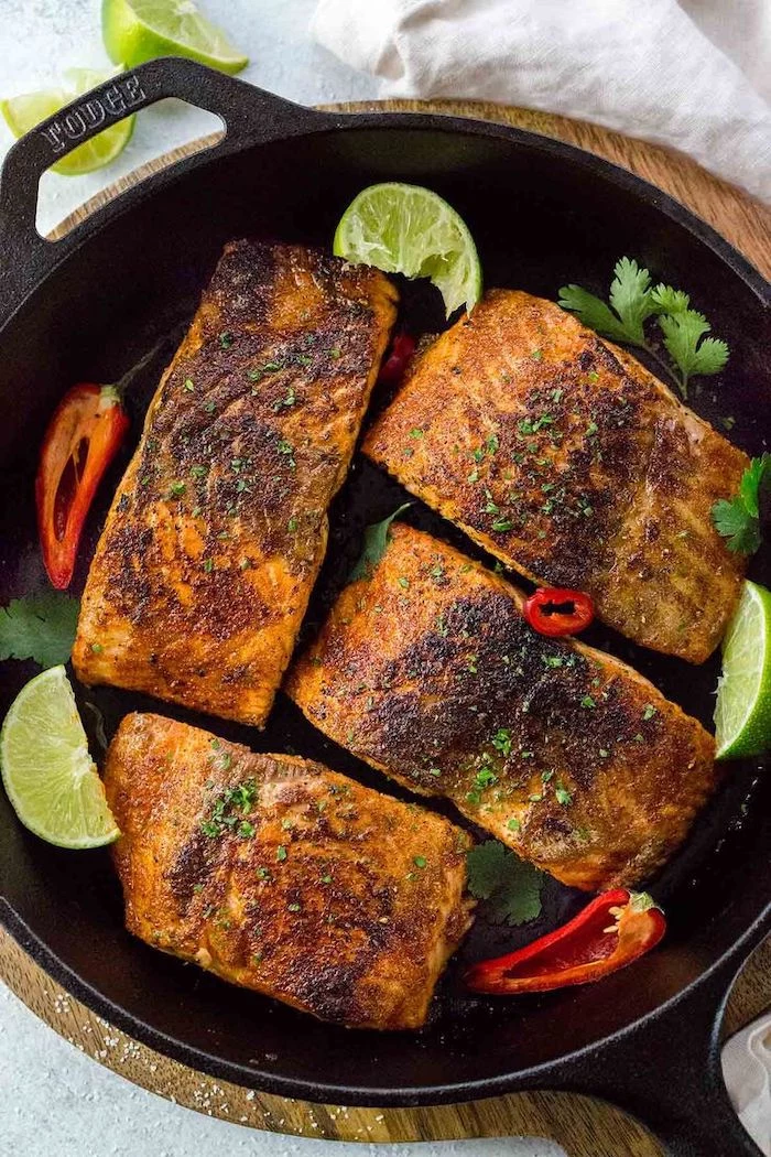 baked salmon, in a black skillet, with sliced peppers, lime slices, low calorie meals, parsley garnish