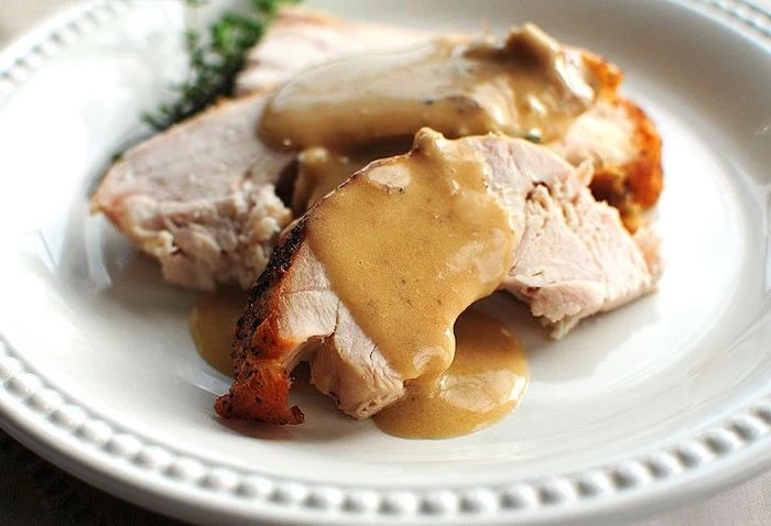 turkey slices, covered in gravy, how to cook a turkey, white plate, fresh herbs