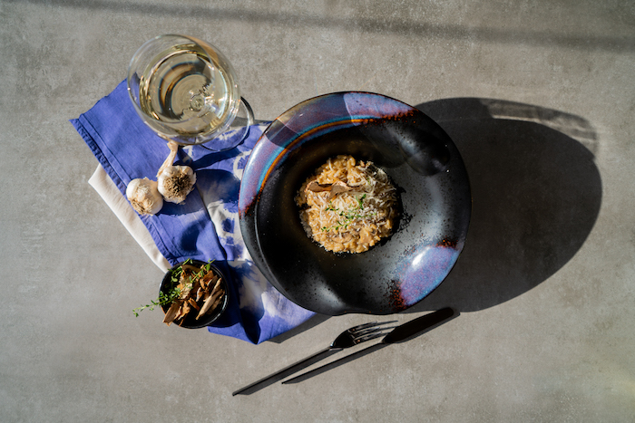 glass of white wine, black bowl with risotto, blue table cloth, arranged on grey surface, mushroom risotto recipe