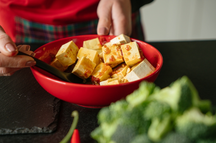 sliced tofu in stirred in sauce, red bowl and black spoon, asian tofu, black cutting board