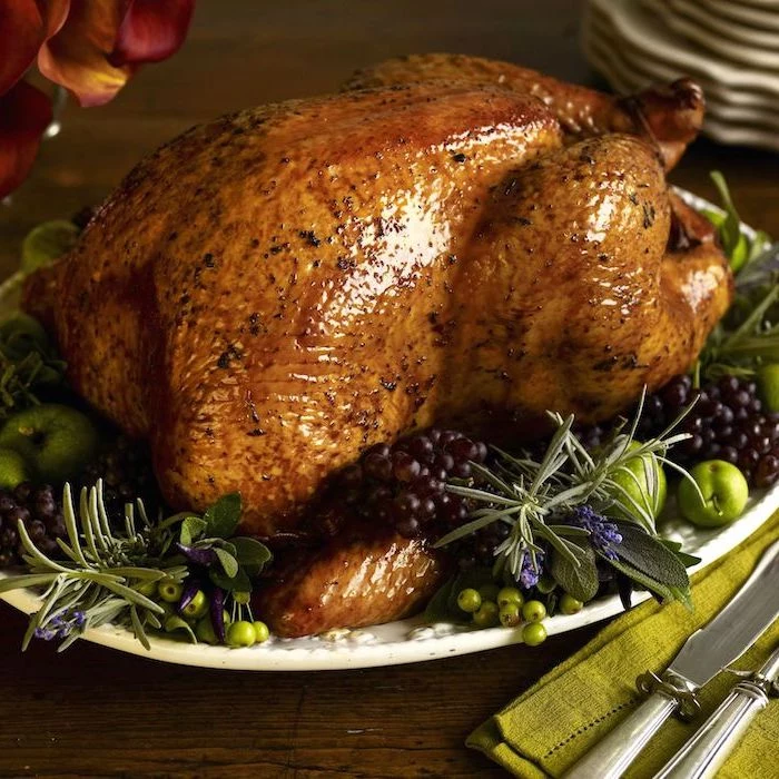 how to bake a turkey, roasted turkey, blackberries and apples, fresh herbs, on the side, wooden table, green cloth