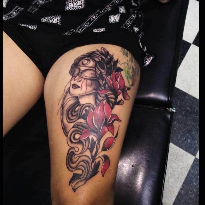 blindfolded women, red flowers, intertwined in her hair, flower thigh tattoo, black leather chair, black shorts