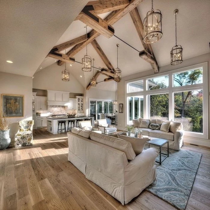 white sofas, wooden floor, blue carpet, hanging lamps, vaulted ceiling beams, kitchen island