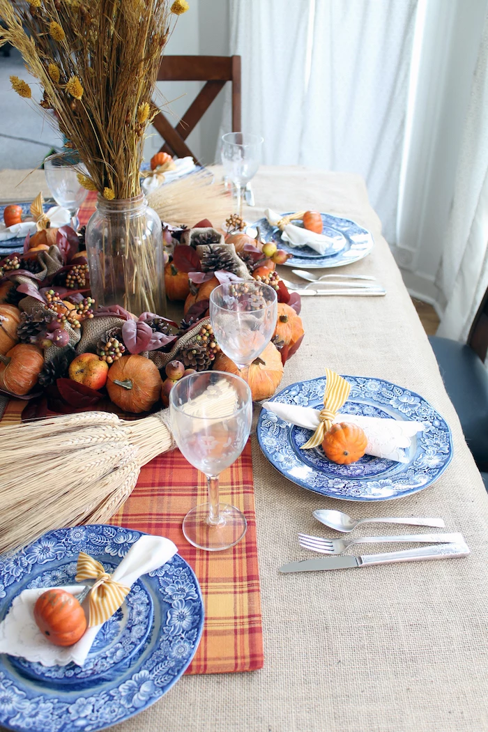 wreath made of pumpkins, pine cones, apples and leaves, thanksgiving decorations, blue plates, wine glasses