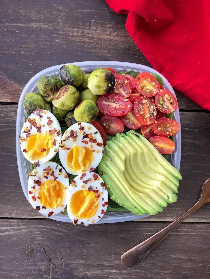 meal prep for weight loss, plastic container, filled with avocado, cherry tomatoes, boiled eggs, wooden table