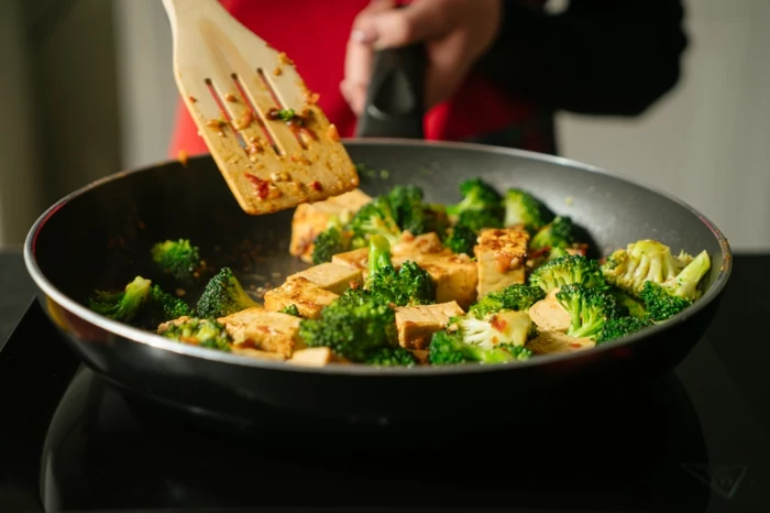 tofu in sauce and broccoli, cooked in black sauce pan, stirred with wooden spatula, asian tofu