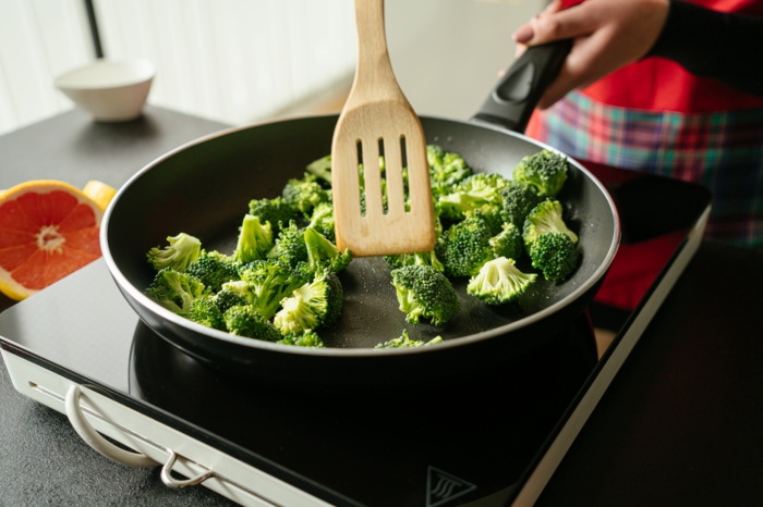 asian tofu recipe, broccoli being cooked in black sauce pan, stirred with wooden spatula