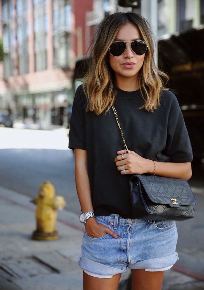 woman wearing sunglasses, denim shorts and black t shirt, medium haircuts for women, brown wavy hair