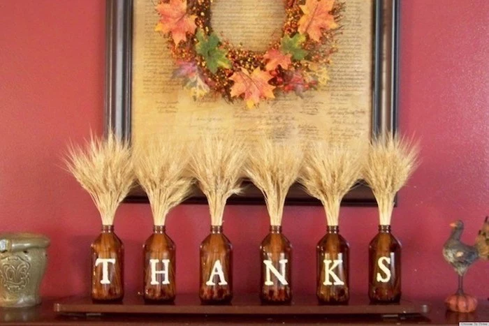 brown bottles, wheat inside, arranged on mantel, thanks written on them, turkey decoration, red wall, fall leaves wreath