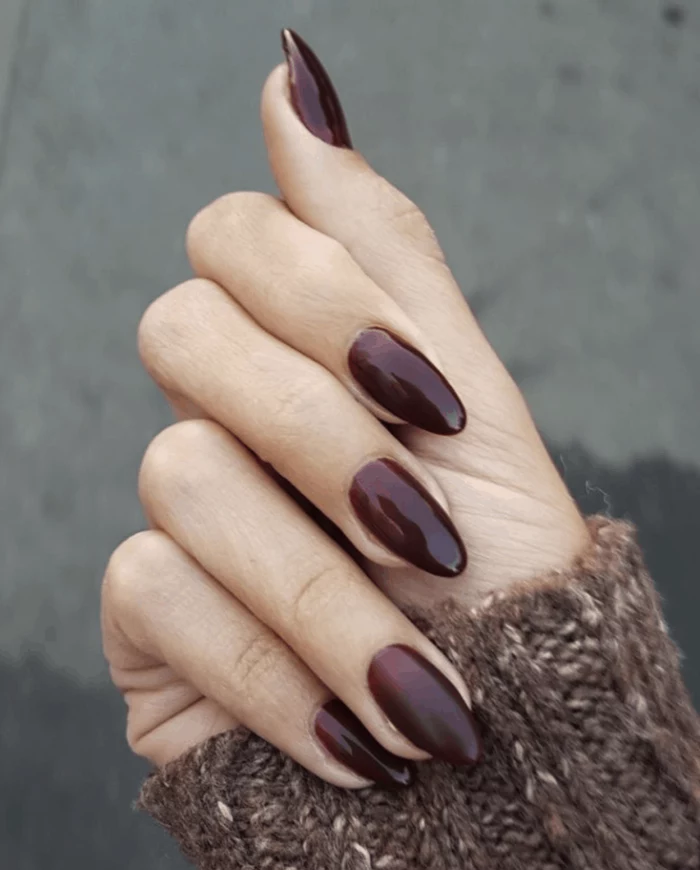 almond nails, trending nail colors, burgundy red, nail polish, brown sweater, blurred background
