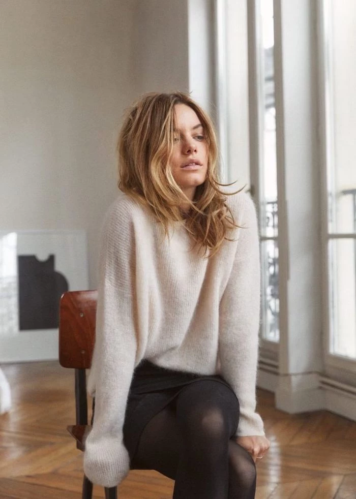 camille rowe sitting on a chair, wearing white sweater and black skirt, medium haircuts for women, wooden floor, white walls