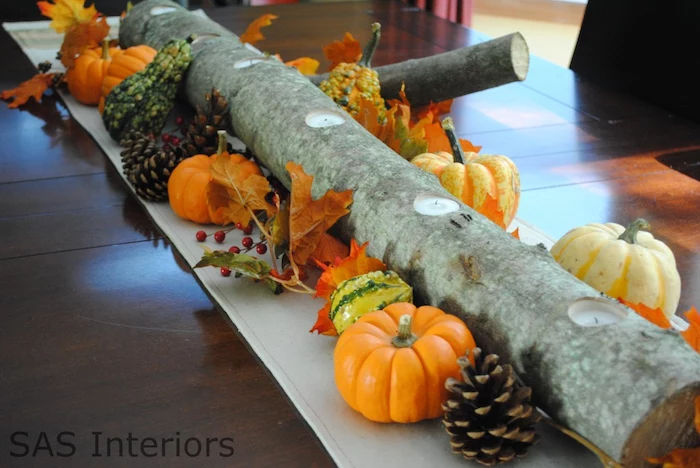 wooden log, candles inside, autumn decor, small pumpkins, pine cones, fall leaves, arranged as table runner