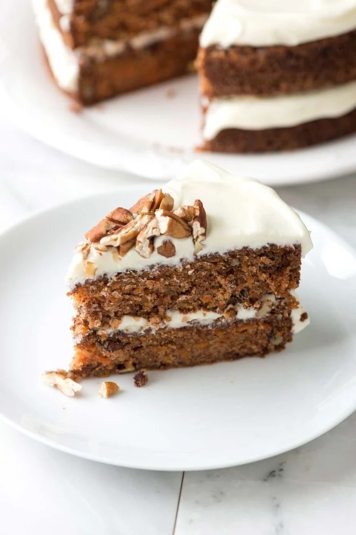 carrot cake, white frosting, crushed walnuts on top, thanksgiving desserts, white plate, marble countertop