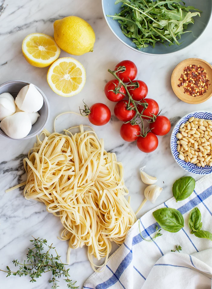 easy dinner ideas, pasta and garlic, basil leaves, cherry tomatoes, lemon slices, bowls full of ingredients, on marble table, 