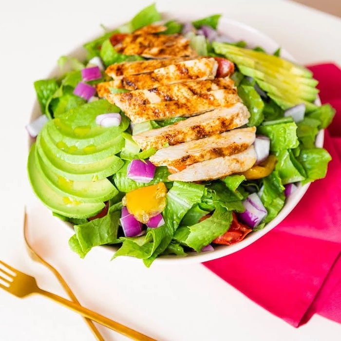 sliced chicken breast, on top of green salad, with avocado slices, red cloth, white plate, meal prep for weight loss