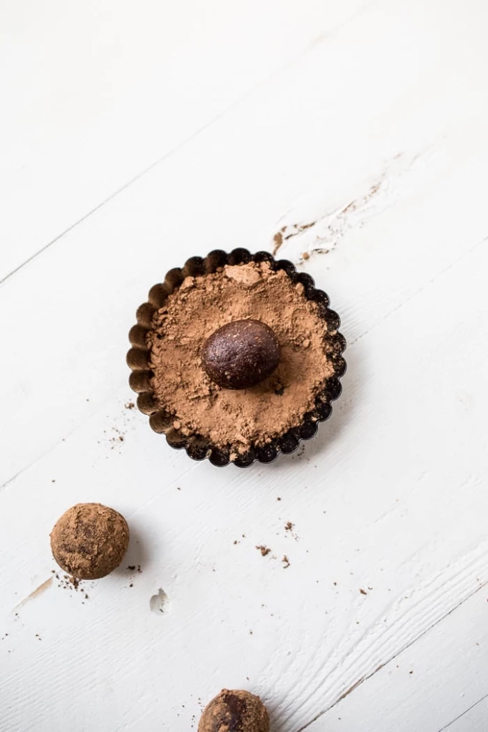 cocoa powder, in a brown ball, healthy peanut butter balls, white wooden table