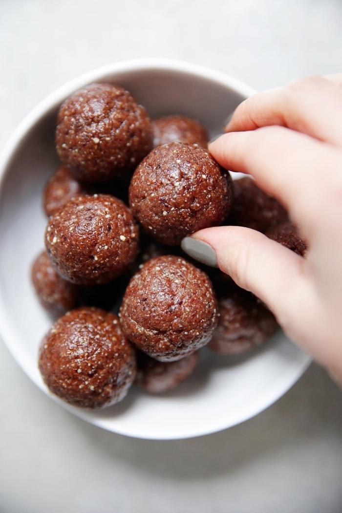 peanut butter energy balls, chocolate truffles, in a white bowl, female hand, with grey nail polish, white table