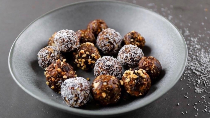 healthy peanut butter balls, covered in nuts, coconut flakes, in grey bowl, coconut flakes, scattered on the table