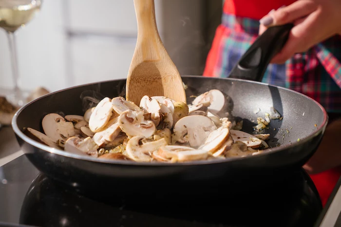 mushrooms stirred with onion, in black sauce pan with wooden spoon, mushroom risotto recipe, blurred background