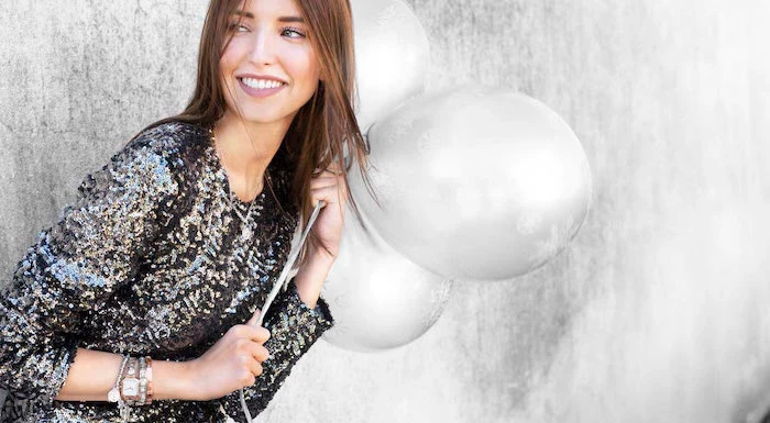 woman holding three balloons, wearing black sequinned dress, lots of bracelets, christmas gift ideas