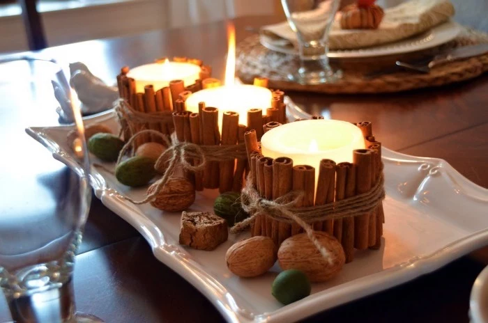 candles with cinnamon sticks, tied with twig, around them, arranged on white plate, thanksgiving decorating ideas, walnuts scattered