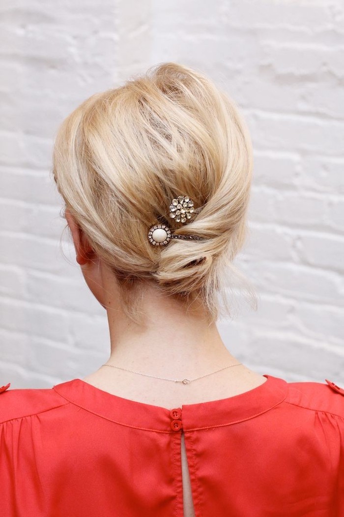 woman with blonde hair, in a low twisted chignon, wearing red dress, medium length hairstyles, white brick wall