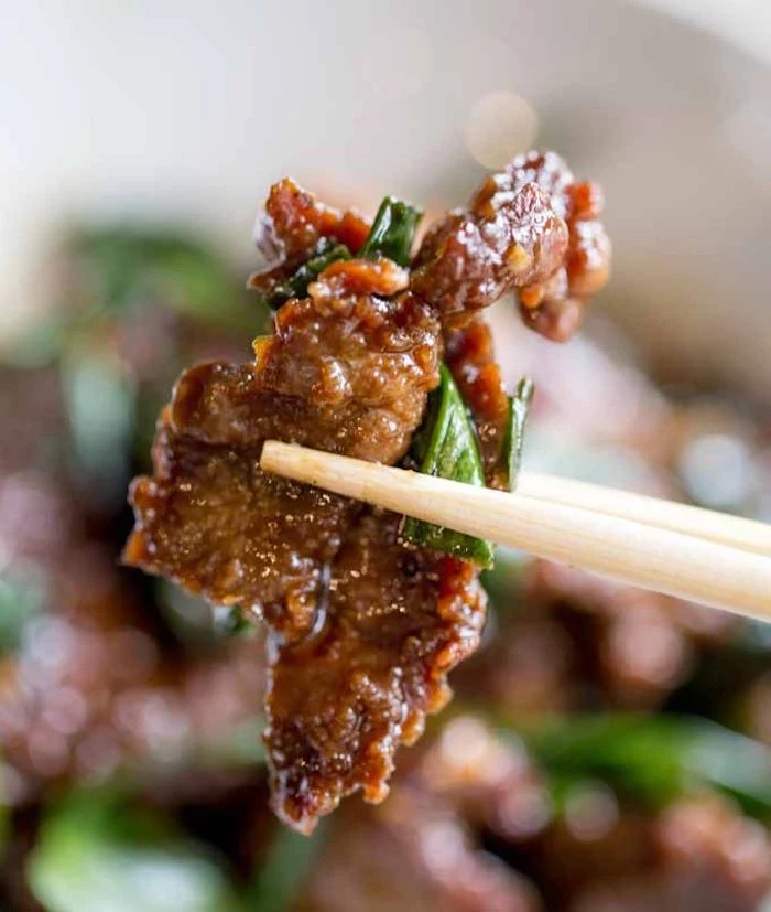 mpngolian beef, cut into pieces, held with chopsticks, what should i make for dinner, blurred background