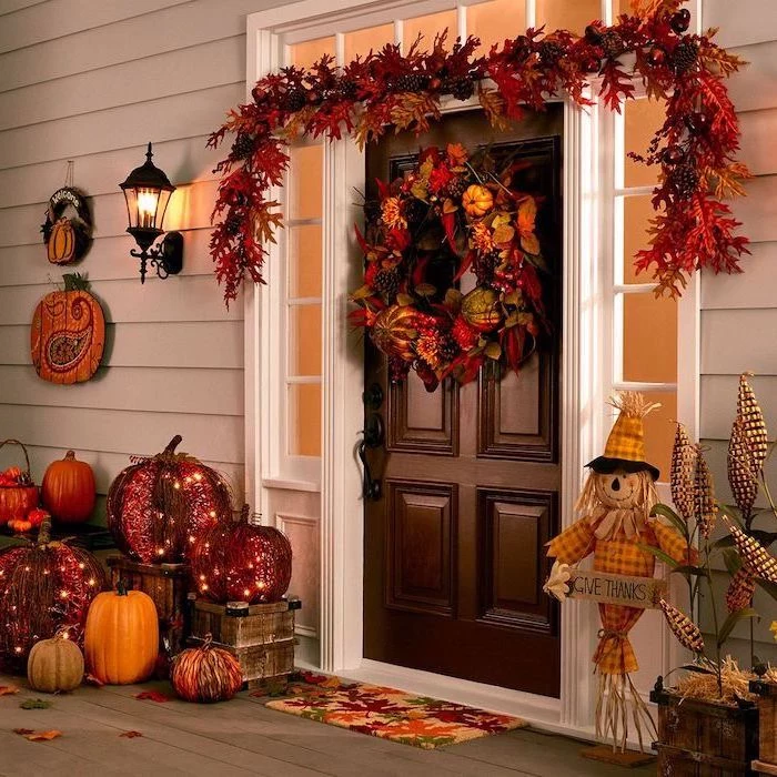 massive wooden door, wreath with autumn leaves, thanksgiving decorations diy, pumpkins arranged around it