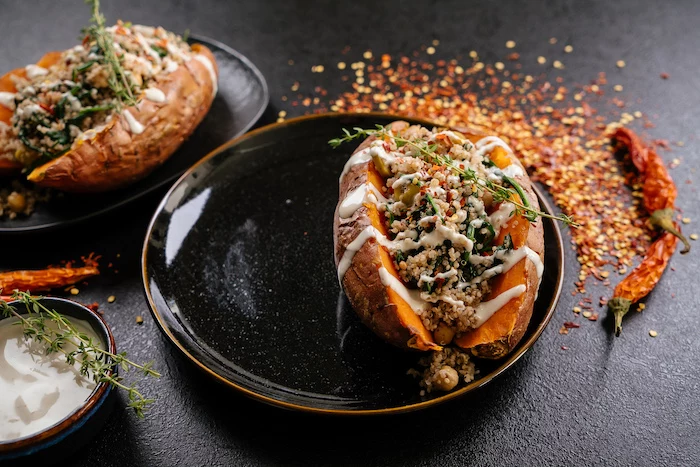 dinner ideas for two, stuffed sweet potatoes, with sauce and thyme for garnish, in black plates, on black table