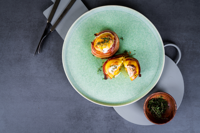 egg filled halved potatoes, wrapped with bacon slices, baked potato volcanoes, arranged on blue plate