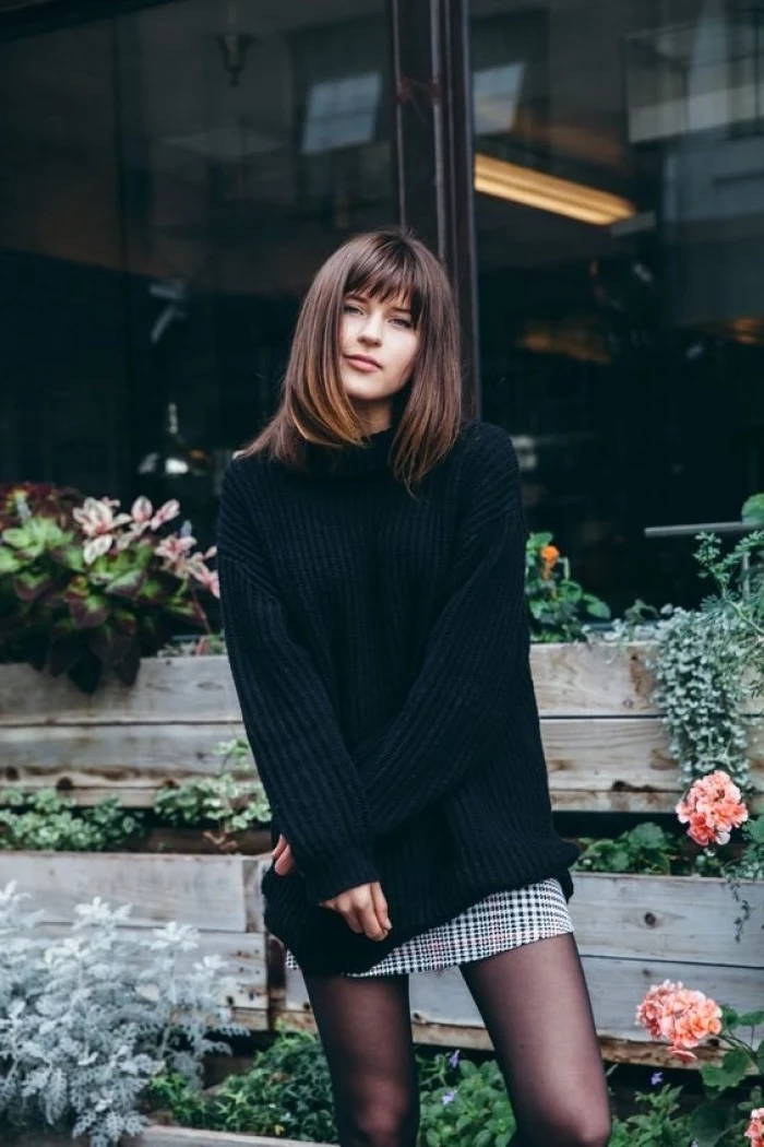 woman wearing black oversized sweater, medium length layered hair, brown hair with bangs, flowers in the background