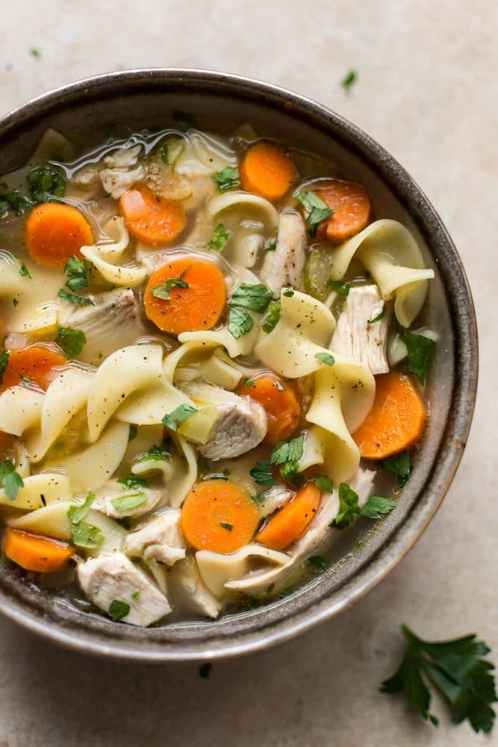 healthy meal prep, turkey noodle soup, chopped carrots, parsley garnish, ceramic bowl