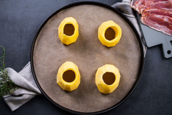 four halved potatoes, insides scooped out, arranged on paper lined sheet pan, baked potato volcanoes, placed on black surface