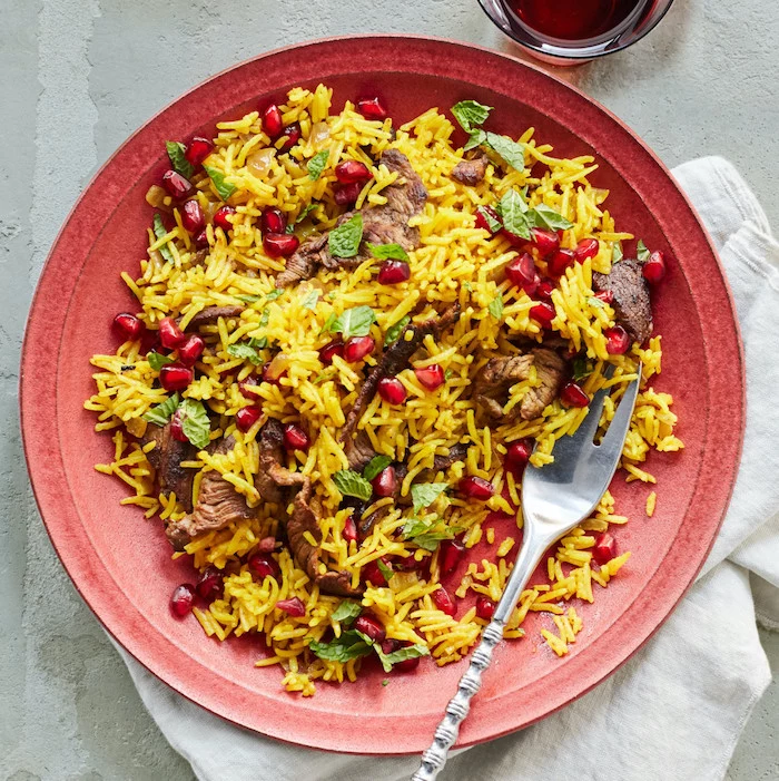 fried rice with steak, what's for dinner tonight, pomegranate seeds for garnish, in red plate, on white table