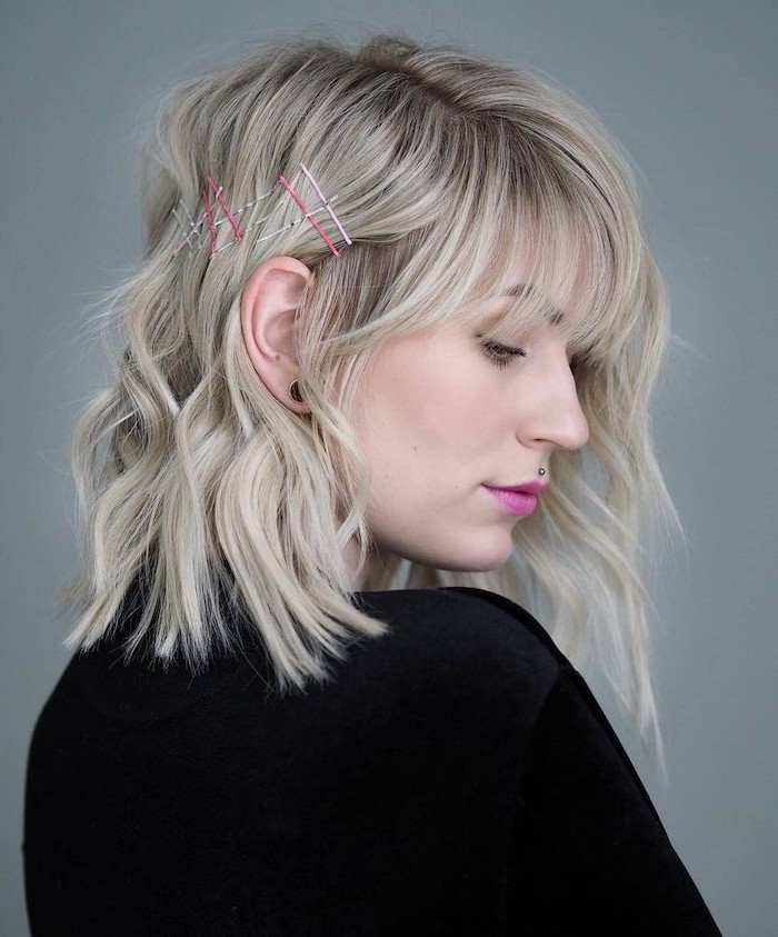 woman with wavy blonde hair with bangs, wearing black blouse, shoulder length hair, pink lipstick