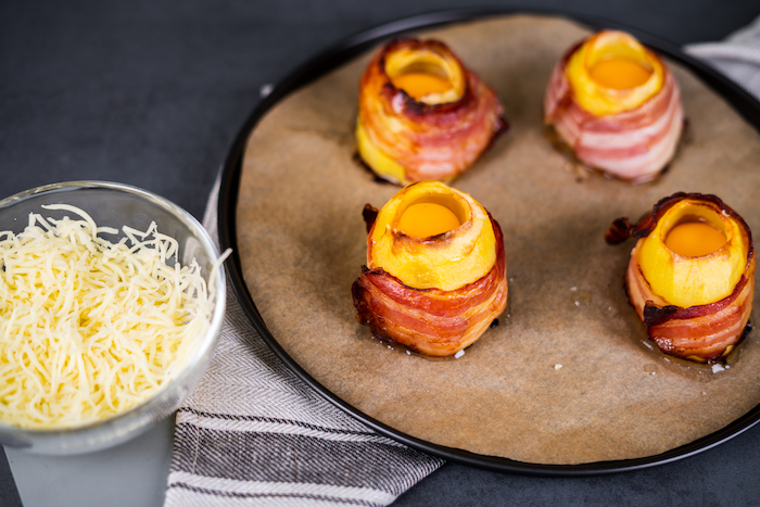 baked potato volcanoes, wrapped with bacon, filled with eggs , arranged on paper lined baking sheet