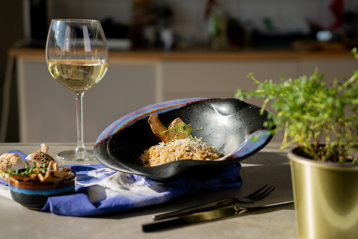 mushroom risotto recipe, risotto placed in black bowl, glass of white wine on the side, topped with fresh thyme and parmesan