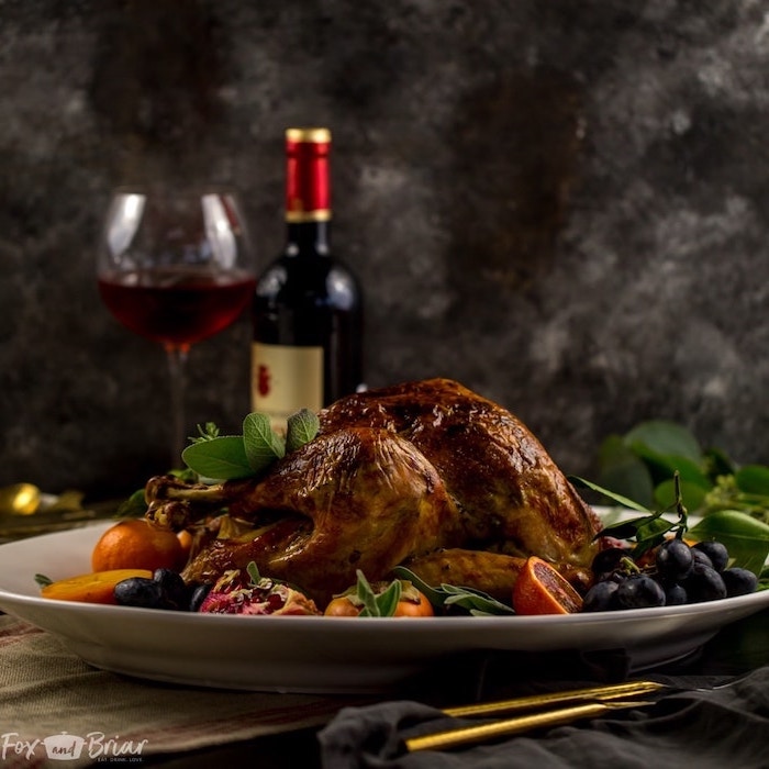 wine glass, wine bottle, oven roasted turkey, grapes and pomegranates, fresh herbs, on the side, white plate