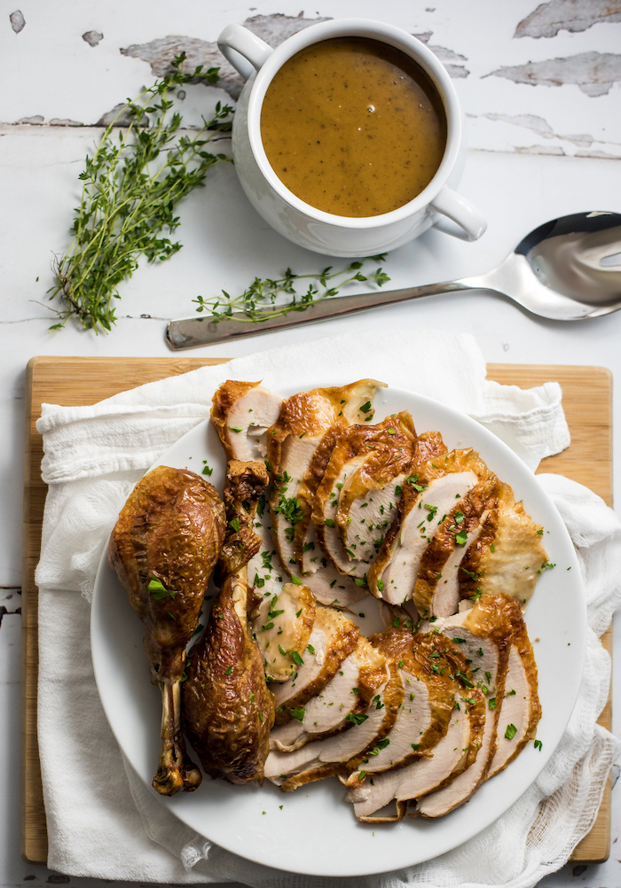 gravy in a jug, carved turkey, white cloth, wooden board, roast turkey recipe, marble countertop, fresh herbs