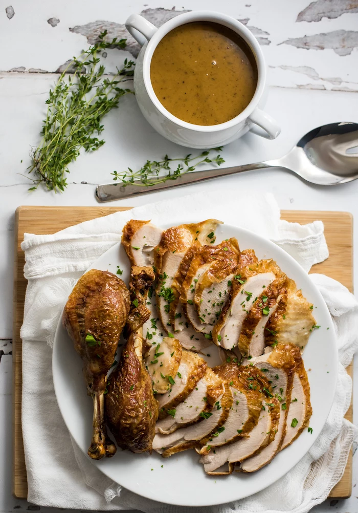 gravy in a jug, carved turkey, white cloth, wooden board, roast turkey recipe, marble countertop, fresh herbs
