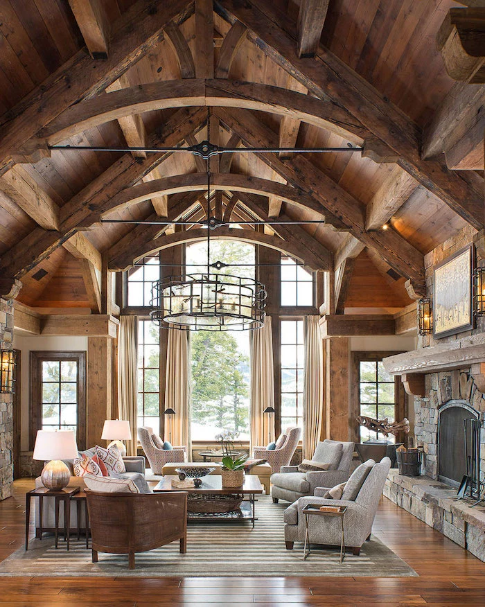 grey armchairs, rustic decor, wooden walls and ceiling, large stone fireplace, cathedral ceiling, tall windows