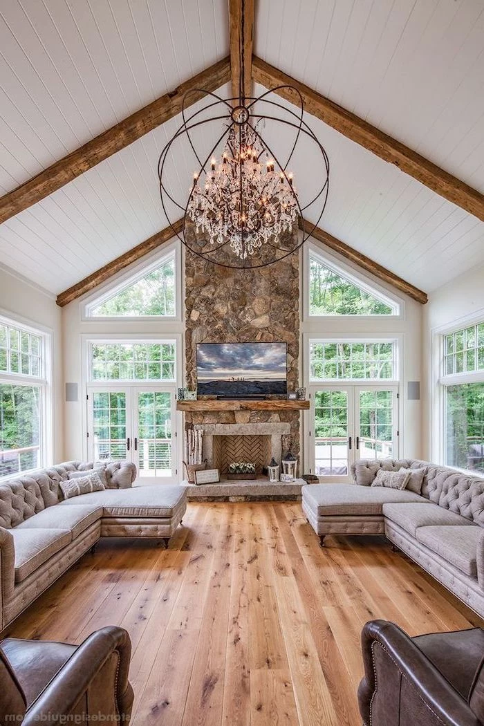 stone fireplace wall, grey corner sofas, brown leather armchairs, wooden floor, vaulted ceiling with beams