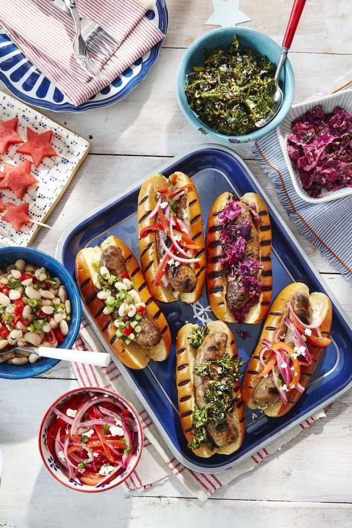 grilled hot dogs, arranged on blue sheet pan, what's for dinner tonight, bowls with different ingredients, white wooden table