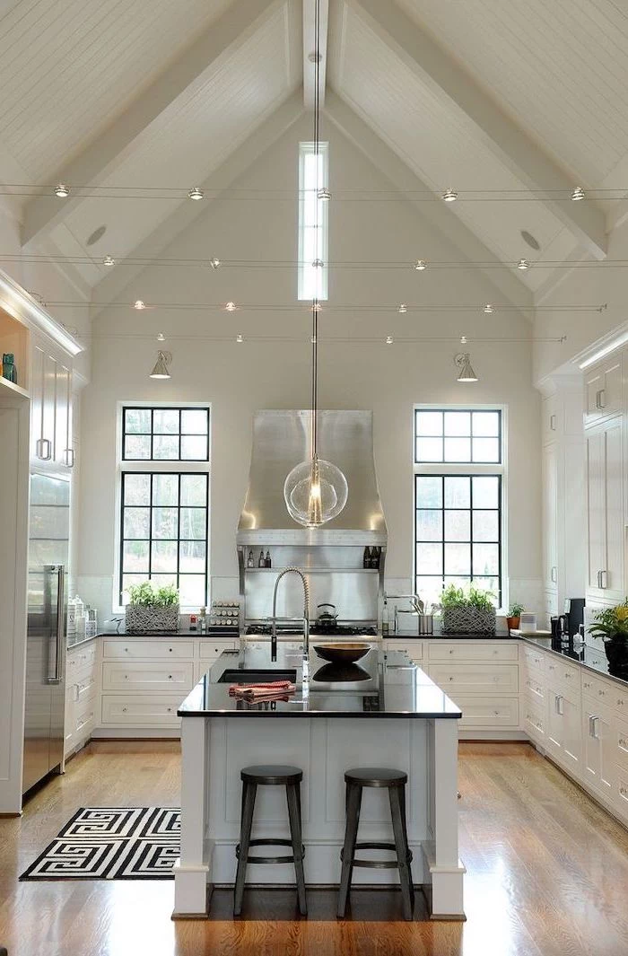 strings of lights, kitchen island, white cupboards, black countertops, vaulted ceiling with beams, wooden floor