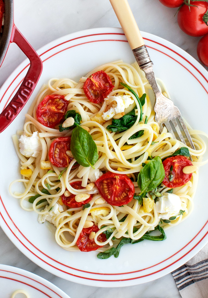 pasta with mozzarella, dried cherry tomatoes, basil leaves for garnish, easy dinner ideas, in white plate, fork on the side